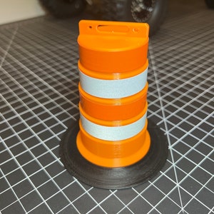 Può includere: Un cono di segnalazione arancione e bianco con una base nera. Il cono è in plastica e ha strisce riflettenti.