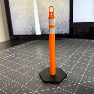 Può includere: Un piccolo cono da traffico arancione con una banda riflettente bianca e una base nera. Il cono è alto circa 25 cm.