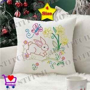 Könnte beinhalten: Weißes quadratisches Kissen mit einem gestickten Osterdesign. Das Design zeigt einen Hasen, einen Schmetterling und Blumen in Rosa-, Blau-, Gelb- und Grüntönen. Auf dem Kissen steht das Wort "STITCH".