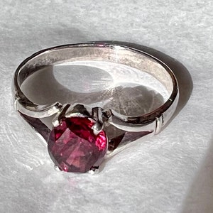 May include: A silver ring with a deep red gemstone set in a delicate, ornate setting.