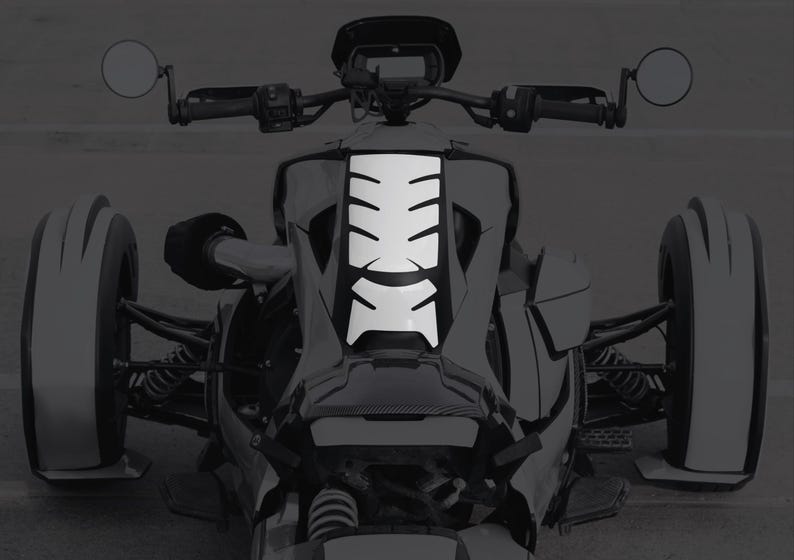 K&ouml;nnte beinhalten: Ein wei&szlig;er Aufkleber mit einem segmentierten Design ist an der Vorderseite eines dreir&auml;drigen Motorrads angebracht. Das Motorrad hat schwarze Lenker, Spiegel und Reifen. Das Bild ist in Graustufen.