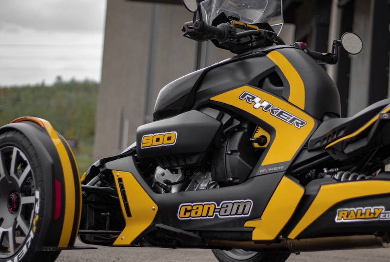 K&ouml;nnte beinhalten: Ein schwarzes und gelbes Can-Am Ryker 900 Dreirad-Motorrad mit einem schwarz-wei&szlig;en "Can-Am"-Logo und dem Text "Ryker" an der Seite.
