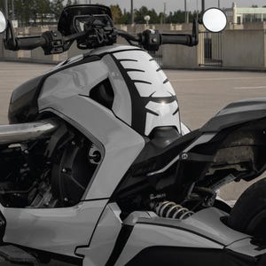 K&ouml;nnte beinhalten: Ein modernes dreir&auml;driges Motorrad in Wei&szlig;- und Schwarzt&ouml;nen. Das Fahrzeug zeichnet sich durch ein einzigartiges Design mit einer stromlinienf&ouml;rmigen Karosserie, runden Spiegeln und einer markanten Frontverkleidung mit schwarzen Akzenten aus. Das Motorrad steht auf einer Asphaltfl&auml;che.