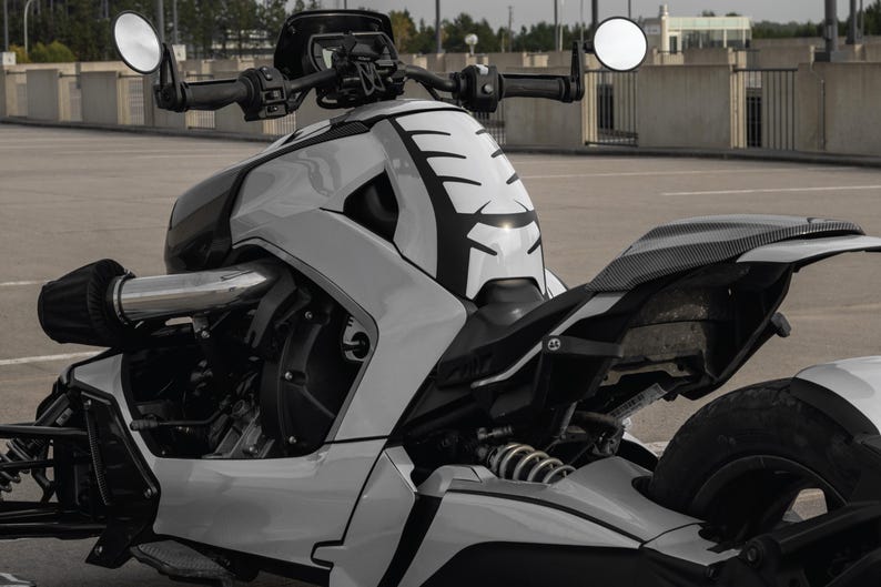 K&ouml;nnte beinhalten: Ein modernes dreir&auml;driges Motorrad in Wei&szlig;- und Schwarzt&ouml;nen. Das Fahrzeug zeichnet sich durch ein einzigartiges Design mit einer stromlinienf&ouml;rmigen Karosserie, runden Spiegeln und einer markanten Frontverkleidung mit schwarzen Akzenten aus. Das Motorrad steht auf einer Asphaltfl&auml;che.