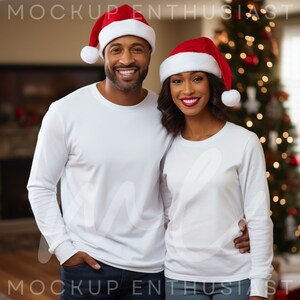 Puede incluir: Una pareja con camisetas blancas de manga larga a juego y gorros de Papá Noel rojos con ribete blanco y pompón blanco. Un árbol de Navidad con luces al fondo. Imagen de Mockup Enthusiast.
