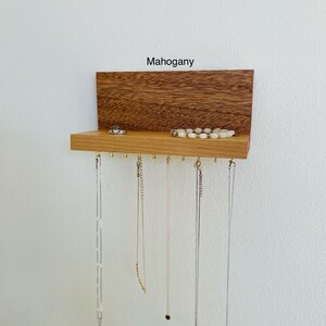 Pu&ograve; includere: Un organizzatore per gioielli in legno di mogano con uno scaffale e ganci per appendere collane. L'organizzatore ha un'etichetta che dice "Mogano".