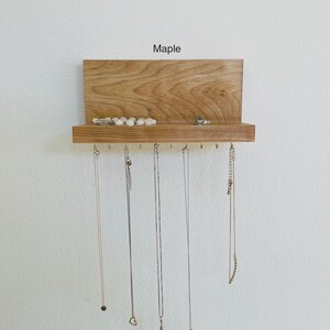 Pu&ograve; includere: Un organizzatore per gioielli in legno con uno scaffale e ganci. L'organizzatore &egrave; in legno d'acero e ha una finitura naturale. Lo scaffale &egrave; utilizzato per riporre anelli e braccialetti, mentre i ganci sono utilizzati per appendere collane.