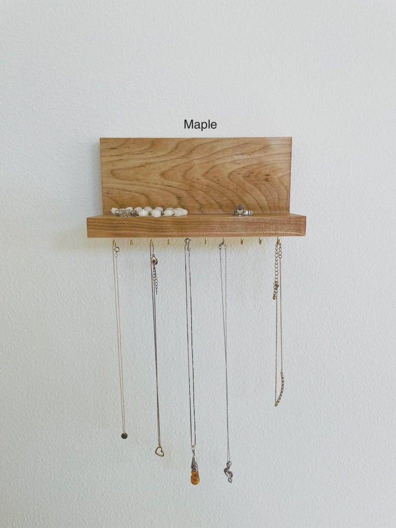 Pu&ograve; includere: Un organizzatore per gioielli in legno con uno scaffale e ganci. L'organizzatore &egrave; in legno d'acero e ha una finitura naturale. Lo scaffale &egrave; utilizzato per riporre anelli e braccialetti, mentre i ganci sono utilizzati per appendere collane.