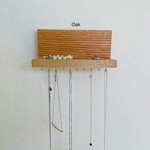 Pu&ograve; includere: Un organizzatore per gioielli in legno con uno scaffale e ganci. L'organizzatore &egrave; realizzato in legno di quercia e ha una finitura naturale. Lo scaffale &egrave; utilizzato per riporre anelli e braccialetti, mentre i ganci sono utilizzati per appendere collane. Il testo "Oak" &egrave; stampato sulla parte superiore dell'organizzatore.