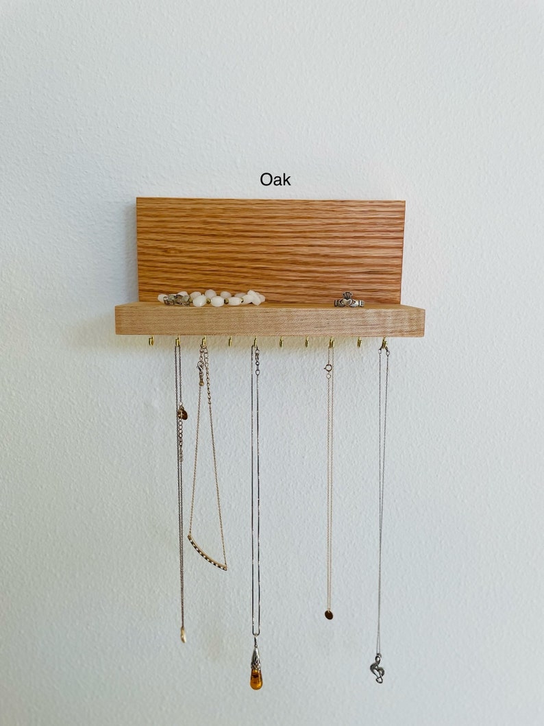 Pu&ograve; includere: Un organizzatore per gioielli in legno con uno scaffale e ganci. L'organizzatore &egrave; realizzato in legno di quercia e ha una finitura naturale. Lo scaffale &egrave; utilizzato per riporre anelli e braccialetti, mentre i ganci sono utilizzati per appendere collane. Il testo "Oak" &egrave; stampato sulla parte superiore dell'organizzatore.