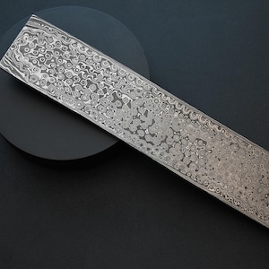 May include: A close-up of a long, silver metal bar with a swirling, patterned surface. The bar is lying on a black surface.