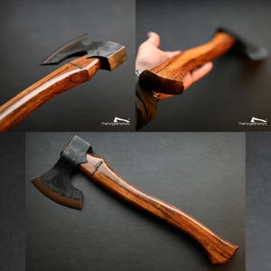 May include: Axe with a dark metal head and a polished wooden handle. The handle is a rich brown color, and the axe head has a curved blade. The axe is displayed against a dark background. The text "TheForgedFactory" is visible.