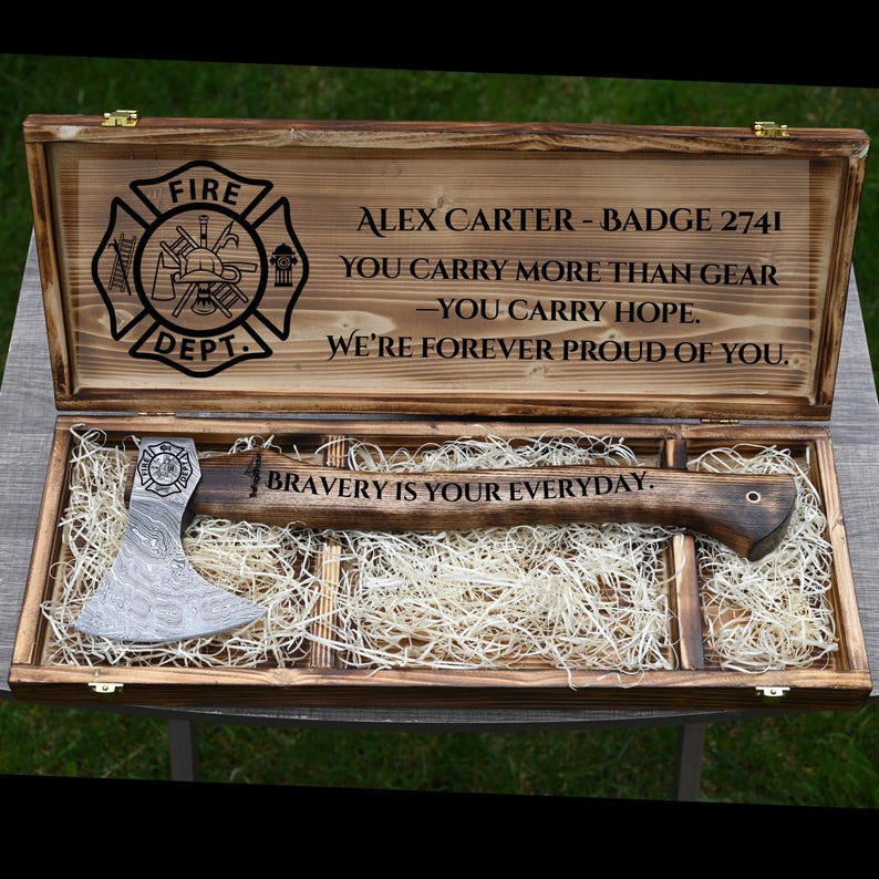 May include: A wooden box with a personalized axe inside, designed for a firefighter. The box lid is engraved with the words "ALEX CARTER - BADGE 2741" and a fire department emblem. The axe has the words "BRAVERY IS YOUR EVERYDAY" engraved on it.