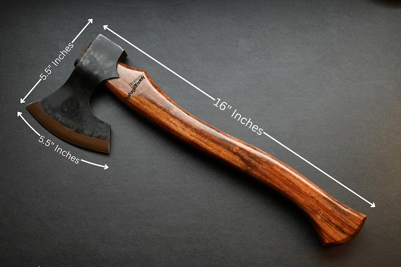 May include: A handcrafted axe with a dark metal head and a wooden handle. The axe head is 5.5 inches wide, and the handle is 16 inches long. The axe has a curved handle and a dark finish, suitable for outdoor activities.