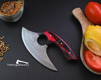 May include: A Damascus steel chef's knife with a red and black wood handle. The knife has a unique curved blade with a hole in the handle. The knife is on a black background with spices and vegetables in the background.