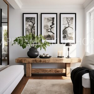 May include: A rustic wooden bench with a black vase filled with green leaves and a bowl of white stones. Three black framed prints with black and white photos of trees hang on the wall above the bench. A black lamp with a white shade sits on the bench.