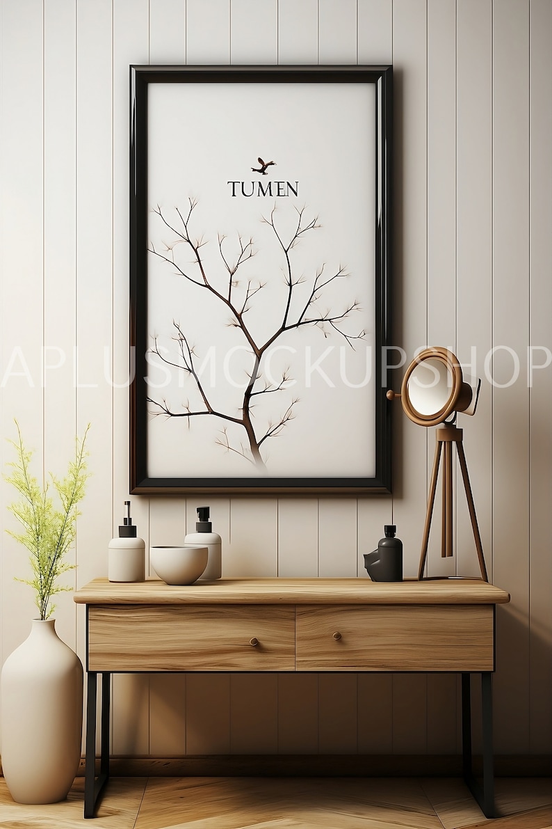 May include: A black framed print with a white background and a stylized tree branch design. The print has the word "TUMEN" in black text. The print is hanging on a white wall above a wooden console table with two drawers. The console table has black metal legs and is decorated with two white pump bottles, a white bowl, a black bottle, and a wooden tripod lamp with a round white shade.