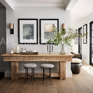 May include: A rustic wooden console table with two metal stools. The table has a distressed finish and is decorated with candles, a vase of greenery, and two framed abstract art prints.