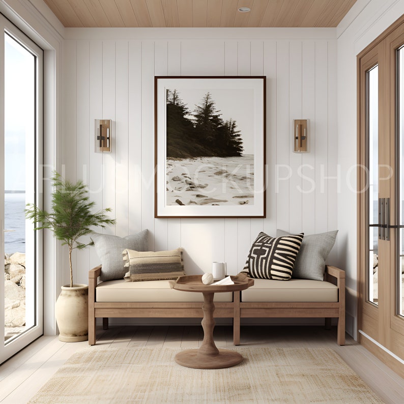 May include: A wooden bench with a beige cushion and two pillows, a brown wooden coffee table with a white mug and a white napkin, a potted plant, and a framed photograph of a beach scene with trees and a snowy shore.
