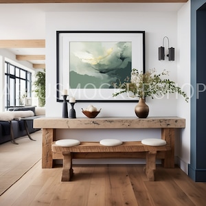 May include: A wooden console table with a rustic finish features a black framed abstract painting above it. The table has a light wood top and two benches with white cushions. A vase with green branches and a bowl of white decorative eggs are on the table.