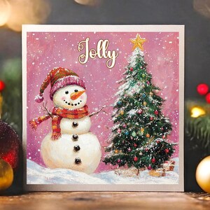 Tarjeta navideña con un alegre muñeco de nieve cuadrado de color rosa que presenta un árbol de Navidad. Disponible como tarjeta individual o en un paquete de 12.