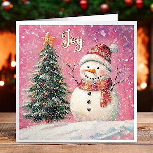 Tarjeta navideña con un muñeco de nieve rosa y un árbol de Navidad. Disponible como tarjeta individual o en un paquete de 12.