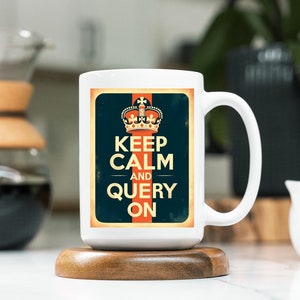 May include: White ceramic mug with a vintage-style design featuring a crown, the text "Keep Calm and Query On", and a red and orange stripe. The mug is sitting on a wooden coaster.