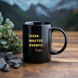 Op de afbeelding: Zwarte koffiemok met de tekst "CLEAN. ANALYZE. OVERFIT. Oops" in gele en oranje letters.