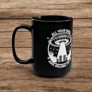 Op de afbeelding: Zwarte koffiemok met een witte afbeelding van een UFO die boven een serverrek zweeft met de tekst "All your data are belong to us".
