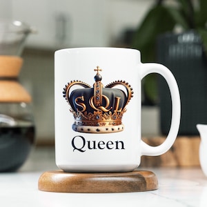 May include: White ceramic mug with a gold crown and the text "SQL Queen" printed on it. The mug is sitting on a wooden coaster.