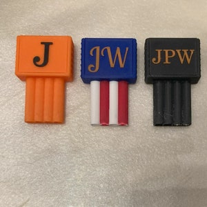 May include: Three rectangular, colorful objects with vertical, ribbed bases. The first is orange with a black "J", the second is blue with gold "JW" and red, white, and red stripes, and the third is black with gold "JPW".