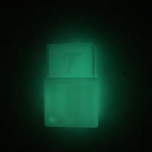 May include: A green glow-in-the-dark wall-mounted key holder with a slot for keys and a small, round button on the bottom. The key holder has the letter "T" printed on the top.
