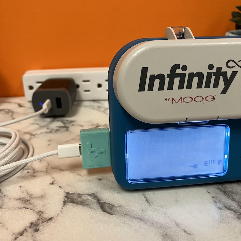 Tubie Tech's USB-C Charger for Infinity Pumps pictured charging a teal Infinity pump with a USB-C to C cable