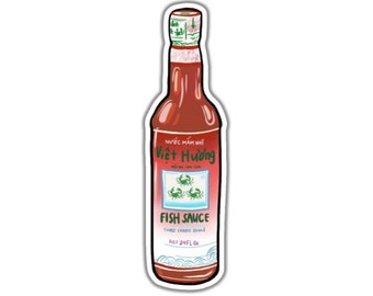 Może przedstawiać: Naklejka z czerwoną butelką sosu rybnego. Na etykiecie widnieje napis "Viet Huong Three Crabs Brand Fish Sauce" z grafiką trzech krabów. Butelka ma 710 ml.