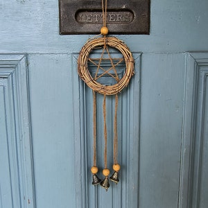 Peut inclure: Un attrape-rêves en brindilles tressées avec un motif d'étoile à cinq branches est suspendu à une porte bleue. Trois petites cloches pendent du bas de l'attrape-rêves.