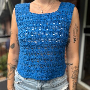 May include: A blue crocheted sleeveless top with a square neckline. The top is made with a delicate open stitch pattern.