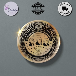 May include: A circular gold-toned medallion featuring the text THE UNITED STATES OF AMERICA, JULY 4th, 1776, DECLARATION OF INDEPENDENCE, and LIFE, LIBERTY, AND THE PURSUIT OF HAPPINESS. It displays three portraits, a scroll, and the Liberty Bell.