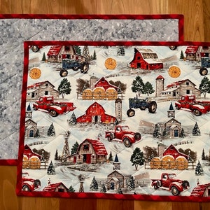 May include: Red and white quilted placemats with a winter farm scene featuring red barns, tractors, trucks, and hay bales. The placemats have a red and white checkered border.