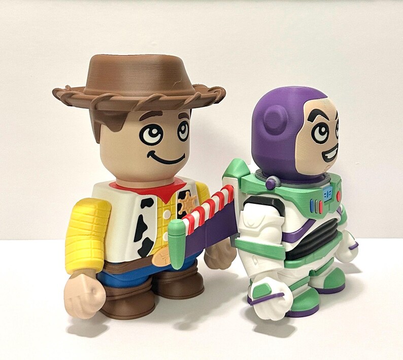 May include: Two stylized toy figures: Woody, in a brown hat, yellow shirt, and blue jeans, and Buzz Lightyear, in a white and green spacesuit with a purple helmet. Both figures have large, smiling faces.
