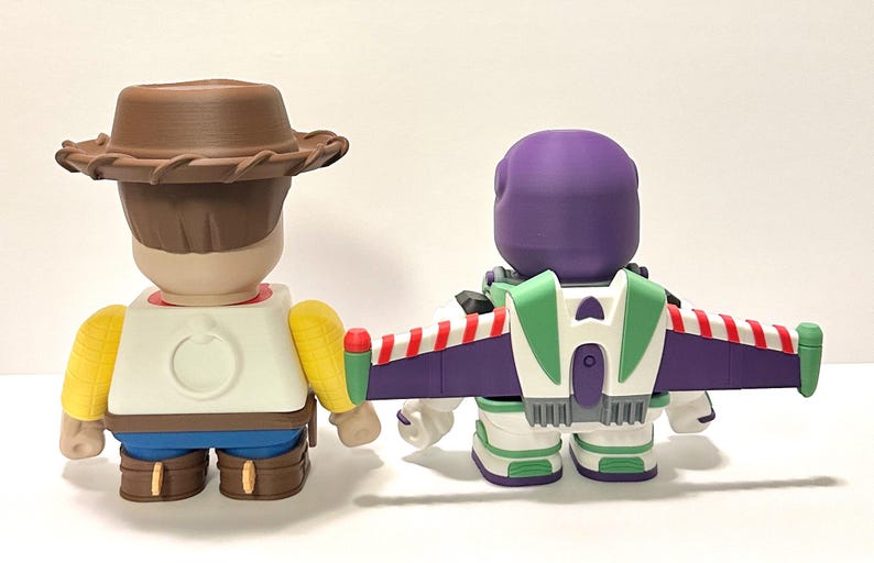 May include: Two collectible figurines, one resembling a cowboy with a brown hat and the other a space ranger with a purple helmet and green and white accents. The space ranger has a purple and white wing pack with red stripes.
