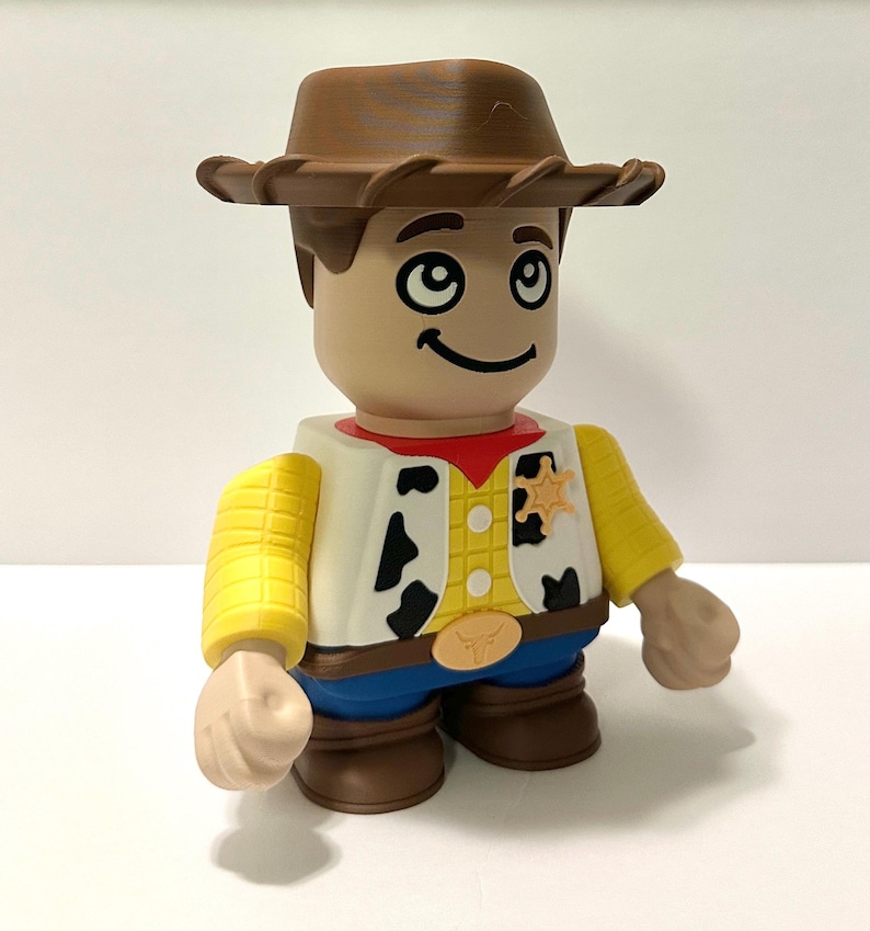 Pu&ograve; includere: Una statuetta di un cowboy con cappello, capelli e stivali marroni. La statuetta ha un viso abbronzato, un gilet bianco con macchie nere, una camicia gialla e pantaloni blu. Un distintivo da sceriffo &egrave; sul gilet.