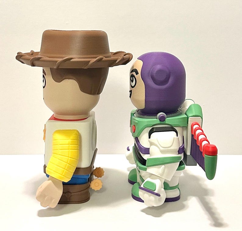 May include: Two stylized figurines of Woody and Buzz Lightyear from Toy Story. Woody wears a brown cowboy hat, a yellow sleeve, and a sheriff's badge. Buzz Lightyear has a purple helmet, green and white spacesuit, and red and white wings.