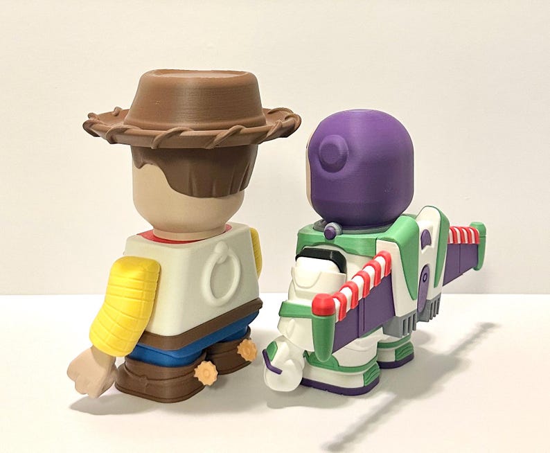 May include: Two collectible figurines: Woody in a brown cowboy hat, yellow shirt, and blue pants, and Buzz Lightyear in a green, white, and purple spacesuit. The toys are from the Toy Story franchise.