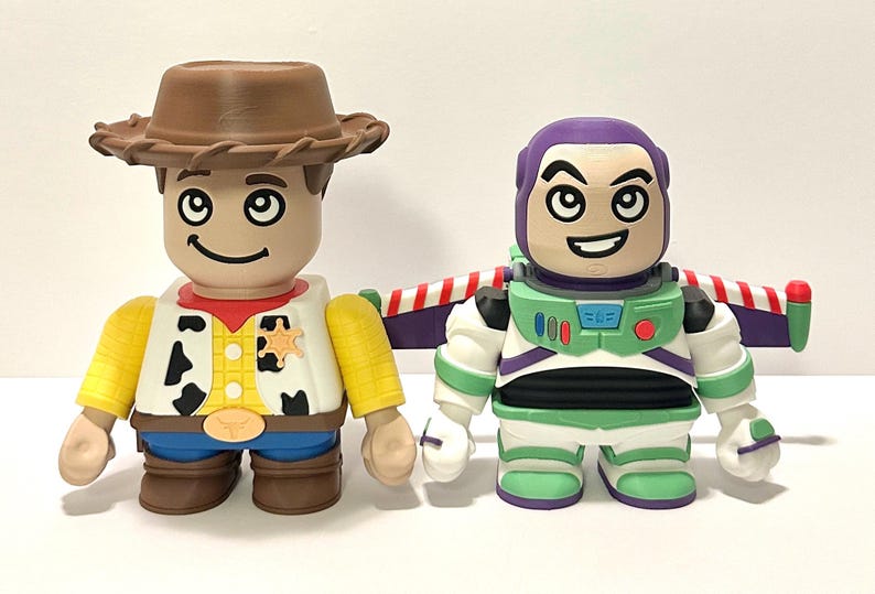 May include: Two collectible figures: Woody, a cowboy with a brown hat, yellow shirt, and blue jeans, and Buzz Lightyear, a space ranger in a green and white suit with purple accents. Both figures have large black eyes and smiling faces.