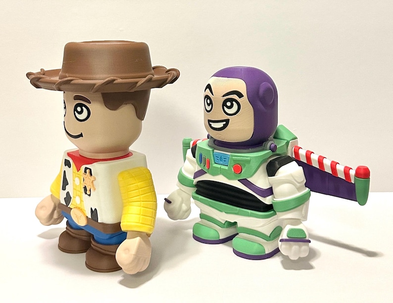 May include: Two collectible figures: Woody, a cowboy with a brown hat, yellow shirt, and blue pants, and Buzz Lightyear, an astronaut in a green and white spacesuit with a purple helmet and wings. Both figures have cartoonish features and are standing side-by-side.