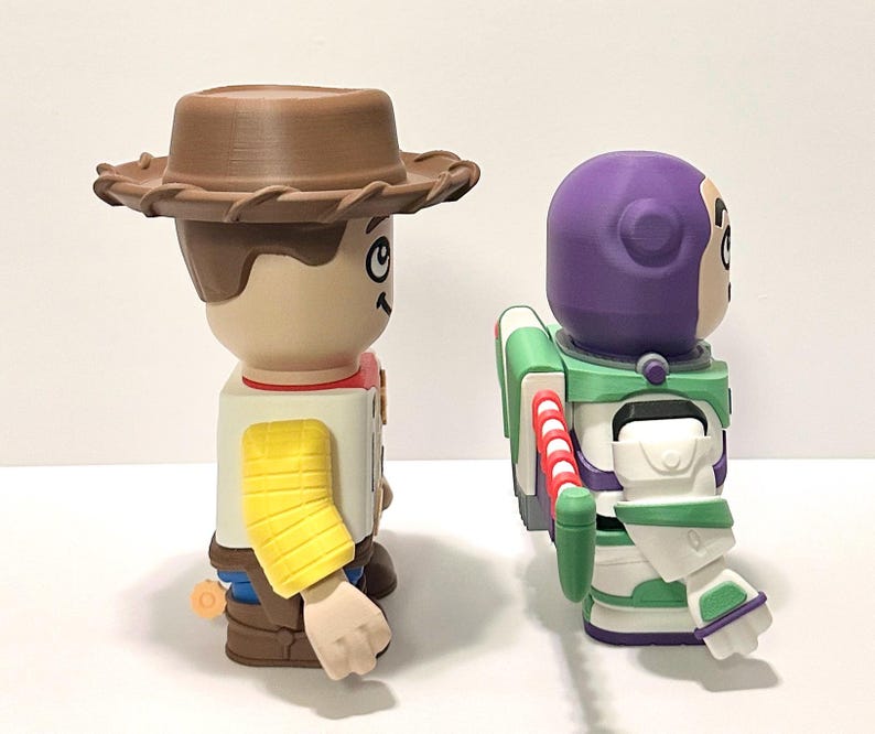 May include: Two character figurines, Woody and Buzz Lightyear, from the animated film Toy Story. Woody wears a brown cowboy hat, a yellow sleeve, and a red neckerchief. Buzz Lightyear has a purple helmet, green and white spacesuit, and red and white jetpack.