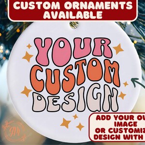 May include: A white, round ornament with the text "YOUR CUSTOM DESIGN" in pink and orange bubble letters. The ornament has a hole at the top for hanging and is decorated with star shapes. Text at the top reads "CUSTOM ORNAMENTS AVAILABLE".