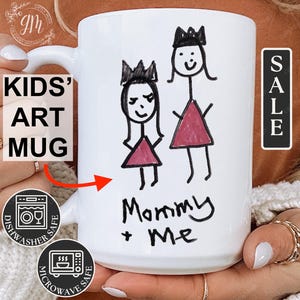 May include: White ceramic mug with a child's drawing of two figures wearing crowns. The drawing is in black marker and says "Mommy + Me". The mug is dishwasher and microwave safe.