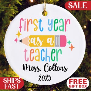 May include: White ceramic ornament with the text "first year as a teacher" in colorful letters, a pencil graphic, and the name "Miss. Collins 2025". Includes a gold hanging loop and the word "SALE" in a red banner.