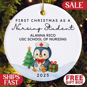 May include: White ceramic Christmas ornament with gold hanging string. The ornament features a penguin in a nurse's hat, a Christmas tree, and a gift. Text reads "First Christmas as a Nursing Student" and "2025".